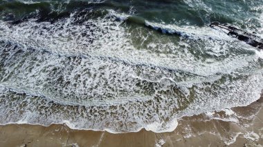 Kumlu sahile yuvarlanan dalgaların üzerinden uçan hava aracı görüntüsü. Üst görünüm