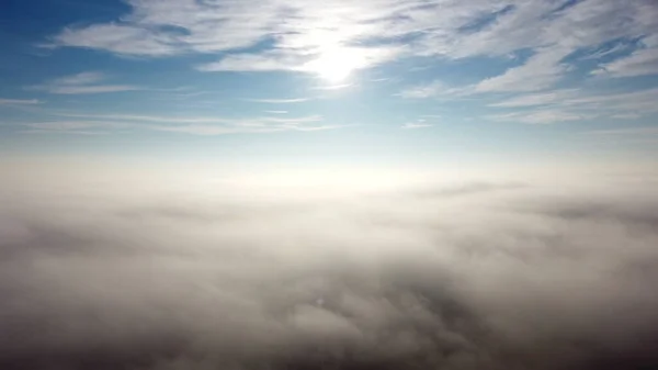 Légi drón kilátás repülés a köd felett és a felhők alatt a ragyogó nap süt. — Stock Fotó