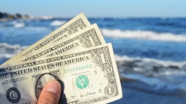 İnsan elinde dalgaların arkasında üç dolarlık banknotlar tutar.