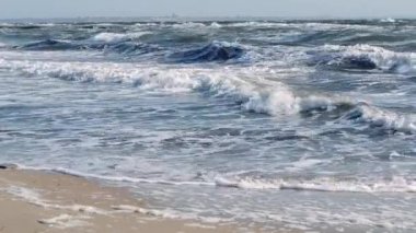 Fırtınalı deniz. Fırtınalı denizin dalgaları güneşli bir günde kıyıda yuvarlanıyor..