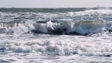 Fırtınalı deniz. Fırtınalı denizin dalgaları güneşli bir günde kıyıda yuvarlanıyor..