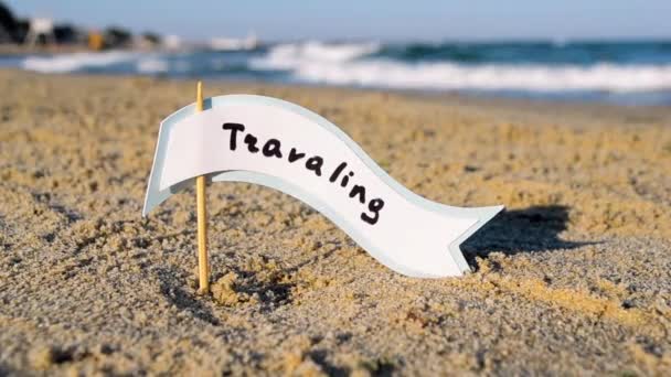 Pequena vara com bolha de fala de papel com palavra Viajar fica na praia arenosa — Vídeo de Stock