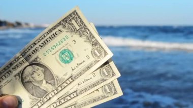 İnsan elinde dalgaların arkasında üç dolarlık banknotlar tutar.