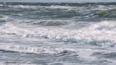 Fırtınalı deniz. Fırtınalı denizin dalgaları güneşli bir günde kıyıda yuvarlanıyor..