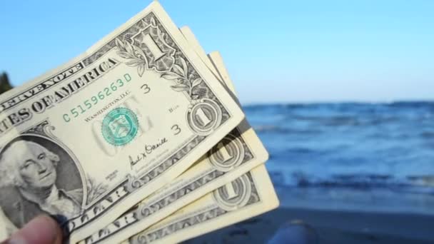 Person håller i sin hand tre dollarsedlar på bakgrunden av vågorna — Stockvideo