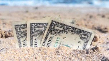 Üç kağıt nakit, bir dolarlık banknotlar. Yarı gömülü, deniz kenarında yakın plan..