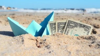 Mavi kağıt tekne ve üç dolarlık kağıt banknotlar. Yarısı kumsalda, deniz kenarında..