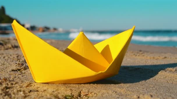 Gele papieren boot op het zand aan de kust tegen de achtergrond van de zee golven — Stockvideo