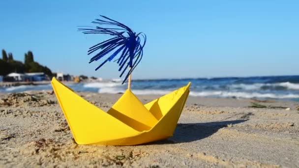 Yellow paper boat on the sand on the seashore against the backdrop of sea waves — ストック動画