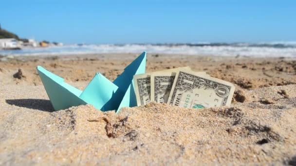 Barco de papel azul y billetes de papel de tres dólares medio en arena en la playa cerca del mar. — Vídeo de stock