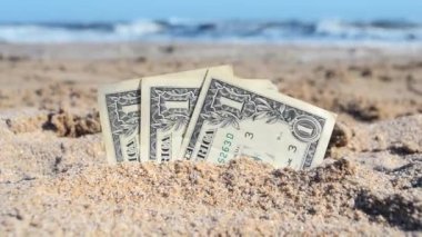 Üç kağıt nakit, bir dolarlık banknotlar. Yarı gömülü, deniz kenarında yakın plan..