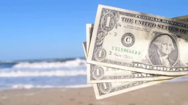 Deniz ve deniz dalgalarının arka planında üç dolarlık banknot tutan kişi