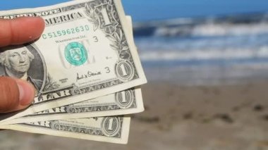 Deniz ve deniz dalgalarının arka planında üç dolarlık banknot tutan kişi