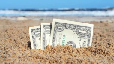 Kağıt, arka planda kumsalda gömülü bir dolar.