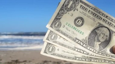 Deniz ve deniz dalgalarının arka planında üç dolarlık banknot tutan kişi