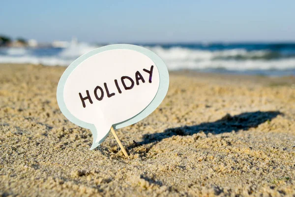 Small stick with paper speech bubble with words Holiday stands on sandy beach — Stock Photo, Image