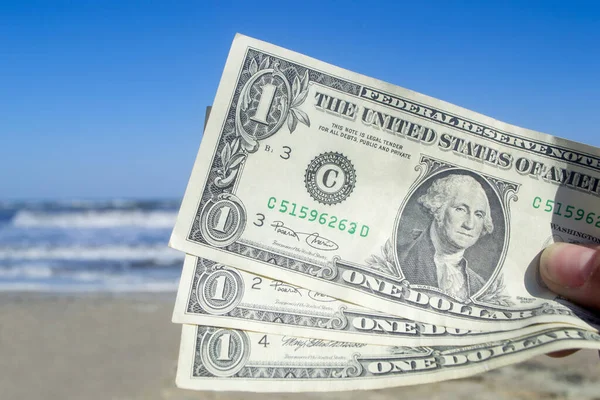 Person holding three paper dollar bills on background of sea and sea waves