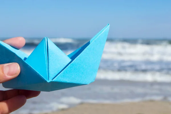 Person holding blue paper boat in hand and playing floating in air on background