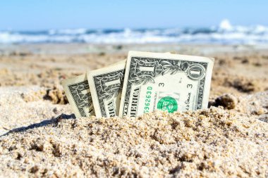 Üç kağıt para bir dolarlık banknotlar, deniz kıyısında kumlara gömülmüş. Kavram para, iş, tasarruf, mali, yatırım, nakit.