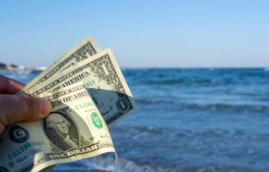 Mavi denizin dalgalarının arka planında bir kişi elinde üç dolarlık banknotlar tutuyor. Konsept para finansman iş turizmi seyahat, para harcamaları, nakit giderler. Para nakit masraf işi