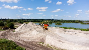Kum madenciliği üzerinde hava aracı görüntüsü. Kum ocağı. Üst Manzara. Kum çukurunun yanında mavi suyu olan bir göl. Taş ocağında kum taşıyan buldozer makinesi. Madencilik endüstrisi. Taş ocağında madencilik ekipmanları.