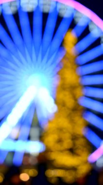 Dönme dolap mavi ışıklandırmayı ve büyük Noel ağacını süsledi. Siyah arka planda sarı ışık vardı. Güzel Yeni Yıl ve Noel tatili arka planda bulanık dikey video