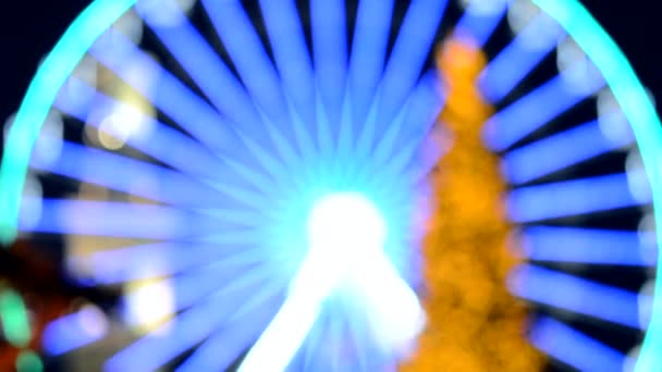 摩天轮上装饰着蓝色的照明 而一棵巨大的圣诞树上装饰着黑色背景的黄色照明 美丽的新年和圣诞假期模糊了背景 — 图库视频影像