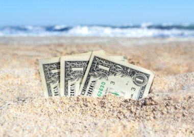 Üç kağıt para bir dolarlık banknotlar, deniz kıyısında kumlara gömülmüş. Kavram para, iş, tasarruf, mali, yatırım, nakit.