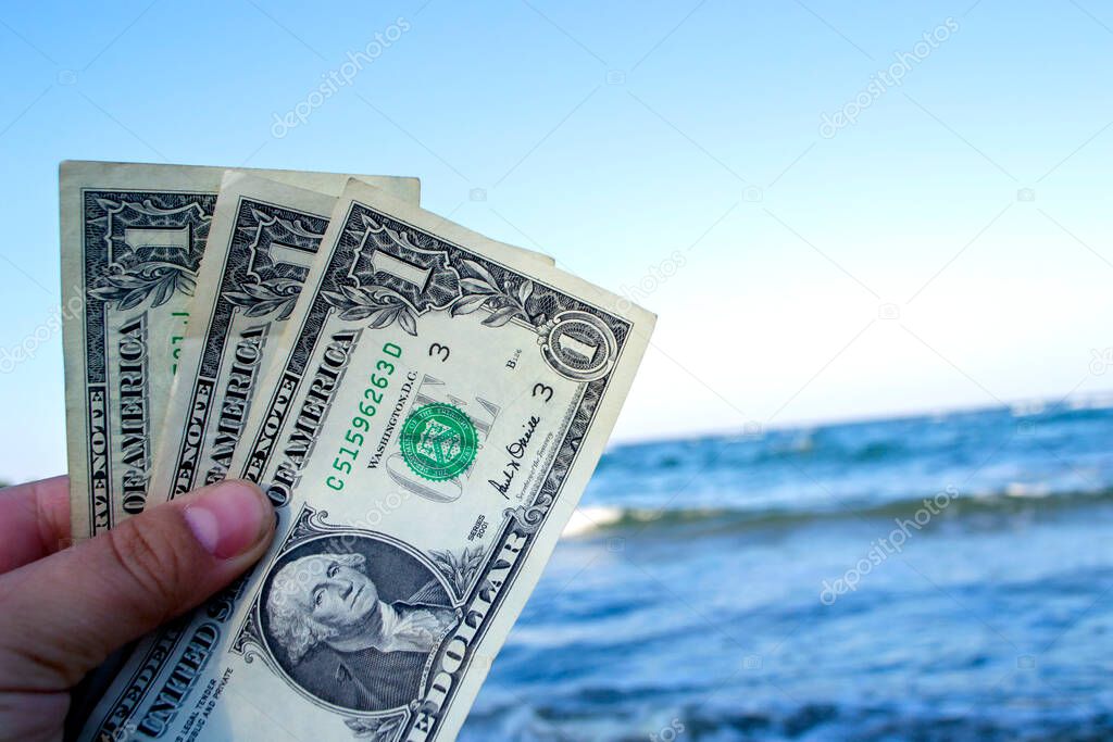 Person holds in his hand three dollar bills on the background of the waves of the blue sea. Concept money finance business tourism travel, money spending, cash expenses. Money cash expenses business