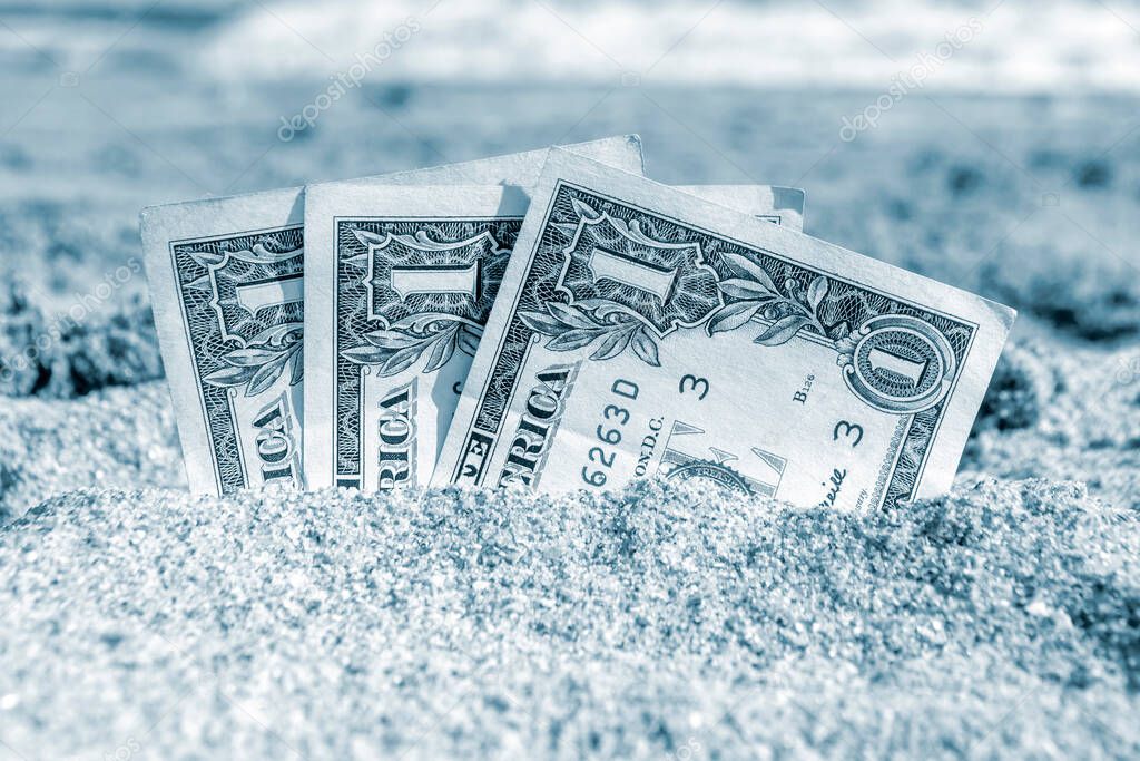 Three paper cash one dollar bills half buried in the sand on the seashore close-up. Concept money, business, savings, financial, investment, cash. Blue color