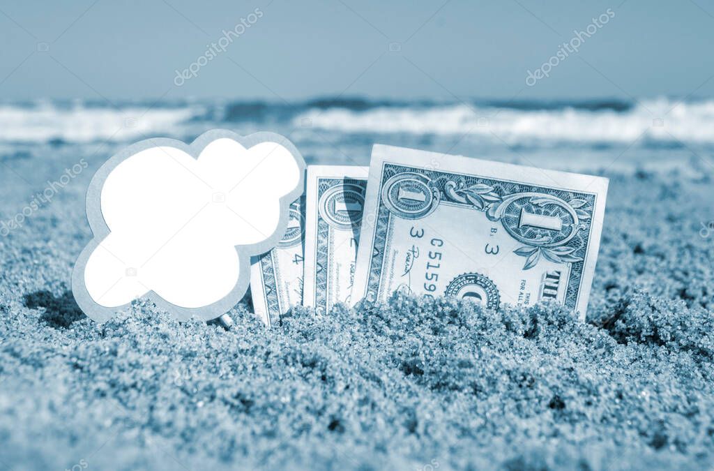 Paper bills one dollar and small stick with clean empty paper speech bubble buried in sand beach background sea close-up in sunny summer day. Concept Money travel tourism vacation. Blue white color
