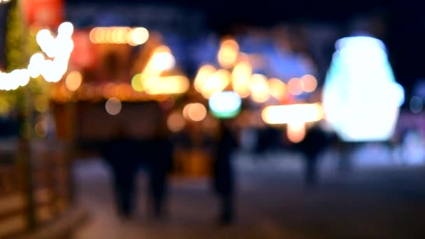 模糊的背景 冬夜人们在城市广场散步 在房屋附近行走的人的黑色轮廓装饰着明亮的照明 从发光的房灯上发出的白光模糊了斑点 — 图库视频影像
