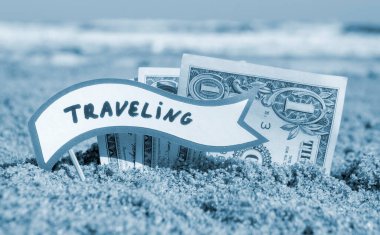 Kağıt bir dolar ve küçük çubuk kağıt konuşma balonu. Kum sahili arka planında, güneşli yaz gününde gömülü. Para seyahati turizm tatili kavramı. Mavi renk