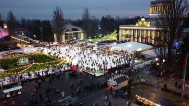 Kiev, Ukrayna, 2 Ocak 2022, güzel şehir manzarası. Birçok insan halka açık şehir parkında kış akşamı aydınlatma ve çelenklerle açık buz pateni pistinde paten kayıyor. Hava Aracı Görünümü