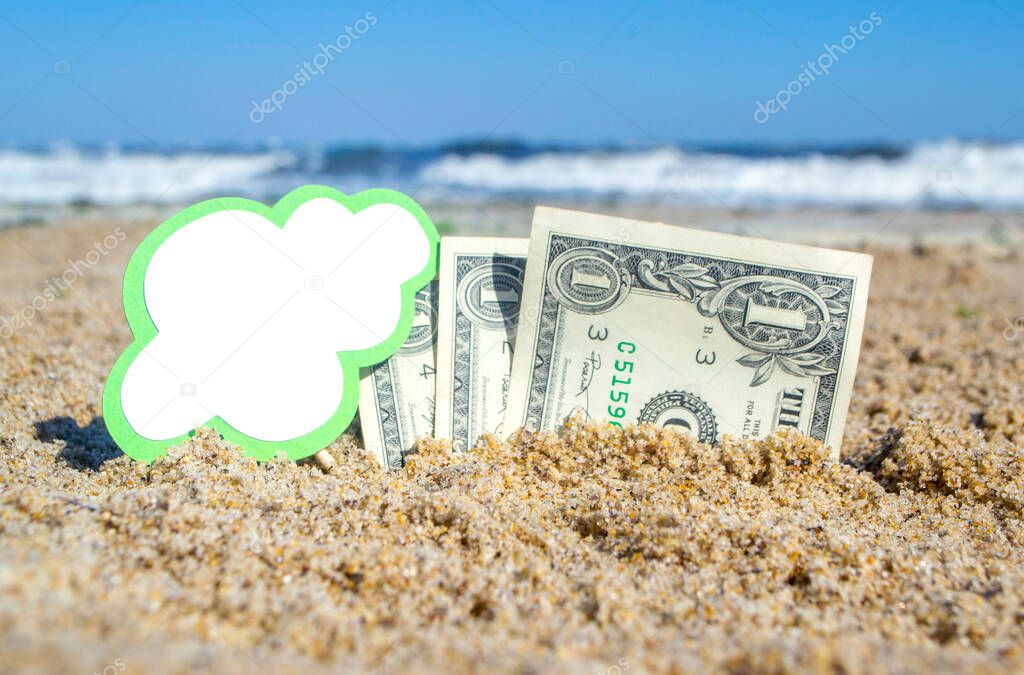 Paper bills one dollar and small green stick with clean empty paper speech bubble buried in sand beach background sea close-up in sunny summer day. Concept Money travel tourism vacation holiday relax