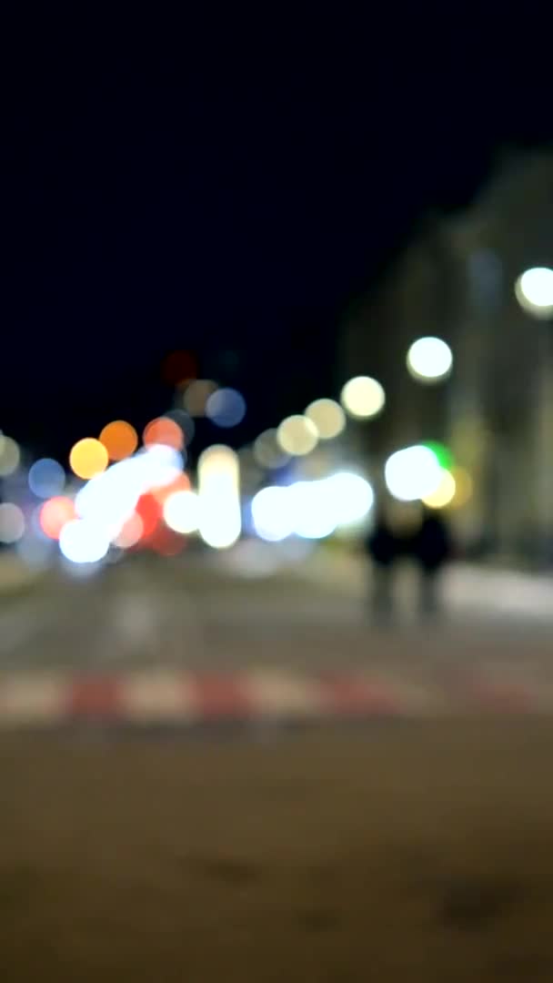 模糊的背景 夜城建筑物轮廓模糊 灯火通明 夜晚街上行走的人轮廓模糊 城市广场漆黑的夜空 垂直录像 — 图库视频影像