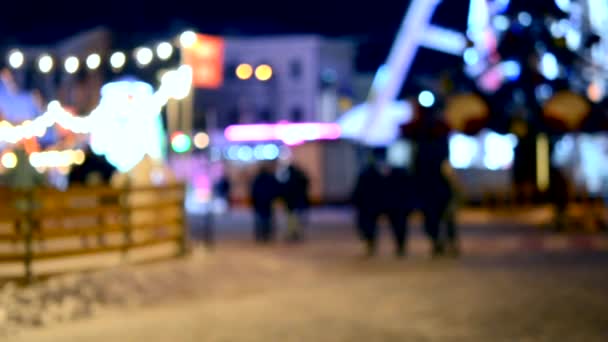 背景がぼやけている 観覧車 輝く光とクリスマスツリー アイスリンク屋外スケートリンク 夜に街の広場を歩く人々のぼやけたシルエット 街のナイトライフ クリスマスタウン — ストック動画