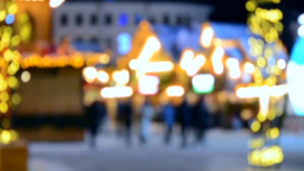 背景がぼやけている 冬の夜にクリスマスタウンの広場を歩く多くの人々のぼやけたシルエット 家の明るい光のガーランドランタンを飾る 点滅するガーランドライト 新年市 — ストック動画