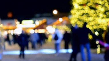 Arka plan bulanık. Noel ağacı, dekore edilmiş parlak ışıklar, bina kış gecesi şehir meydanında yürüyen insanların bulanık siluetleri. Güzel yeni yıl ve Noel tatili geçmişi bulanıklaştırıyor