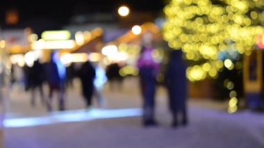 Arka plan bulanık. Noel ağacı, dekore edilmiş parlak ışıklar, bina kış gecesi şehir meydanında yürüyen insanların bulanık siluetleri. Güzel yeni yıl ve Noel tatili geçmişi bulanıklaştırıyor