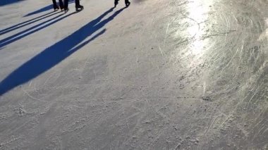 Güneşli kış gününde iki kişi açık havada buz pateni pistinde paten kayıyor. Buz pateni pistinde kayan insanlar. Bacaklar, sırt, gölgeler, güneş ışığı buz pateni pisti. Kış tatili aktiviteleri dinlenme sporu