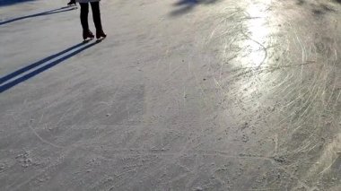 People skating on public open-air ice skating rink in city on sunny winter day. People skating on ice rink. Legs, back, shadows, sunlight ice rink. Winter holidays activities recreation rest sport