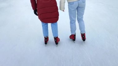 Two people skating on public open-air ice skating rink in city on winter day. People skating on ice rink. Legs, back, ice rink. Winter holidays, activities ,recreation ,rest, sport