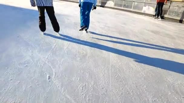在阳光明媚的冬日 两个人在城市露天溜冰场上滑冰 人们在冰场上滑冰 阳光溜冰场 寒假活动休闲活动 — 图库视频影像