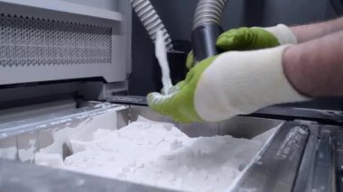 Çalışan bir elektrik süpürgesiyle çalışan bir adam, 3D yazıcının içindeki 3D yazıcıya basılmış bir modeldeki beyaz poliyamit tozunu temizlemek için çalışıyor. Endüstriyel toz 3D yazıcıya basılmış temizleme nesneleri