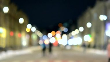 Arka plan bulanık. Gece şehri. Bulanık binalar, parlayan fenerler, akşamları sokakta yürüyen insanların bulanık siluetleri. Şehir meydanı, kara gece gökyüzü