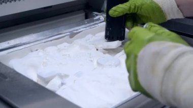 Çalışan bir elektrik süpürgesiyle çalışan bir adam, 3D yazıcının içindeki 3D yazıcıya basılmış bir modeldeki beyaz poliyamit tozunu temizlemek için çalışıyor. Endüstriyel toz 3D yazıcıya basılmış temizleme nesneleri