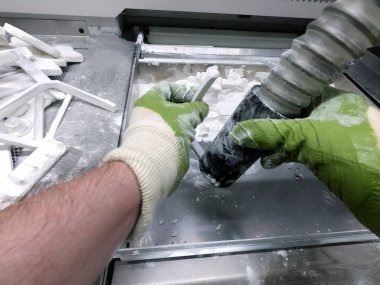 Çalışan bir elektrik süpürgesiyle çalışan bir adam, 3D yazıcının içindeki 3D yazıcıya basılmış bir modeldeki beyaz poliyamit tozunu temizlemek için çalışıyor. Endüstriyel toz 3D yazıcıya basılmış temizleme nesneleri