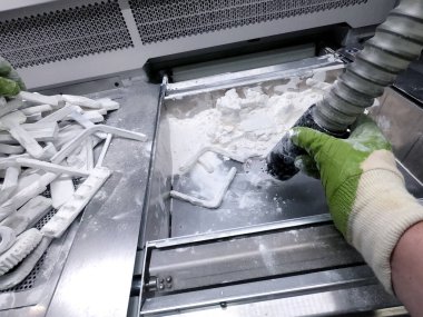Çalışan bir elektrik süpürgesiyle çalışan bir adam, 3D yazıcının içindeki 3D yazıcıya basılmış bir modeldeki beyaz poliyamit tozunu temizlemek için çalışıyor. Endüstriyel toz 3D yazıcıya basılmış temizleme nesneleri