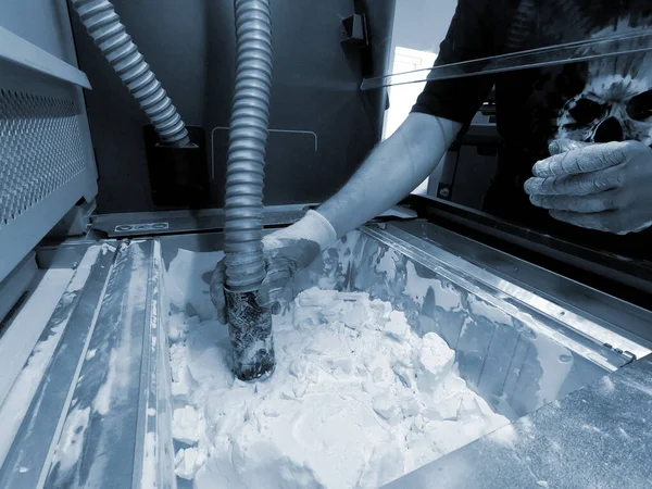 A man working with a working vacuum cleaner to clean the white powder of polyamide from a model printed on a 3D printer inside a 3D printer. Cleaning objects printed on an industrial powder 3D printer